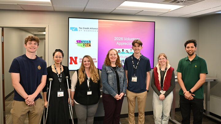 Group of seven volunteers standing in front of a screen displaying '2026 Volunteer Appreciation' with the TCAN, VITA, and CCFL logos in a conference room.