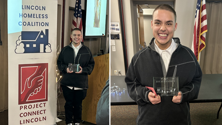 Person holding an award standing next to a Lincoln Homeless Coalition and Project Connect Lincoln banner indoors.