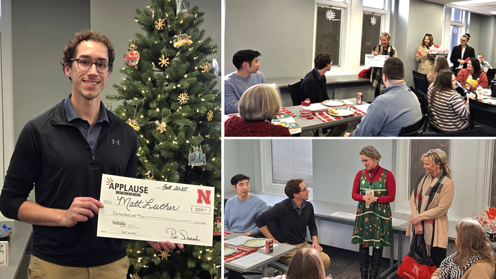 Man holding a large Applause award check standing next to a decorated Christmas tree indoors.